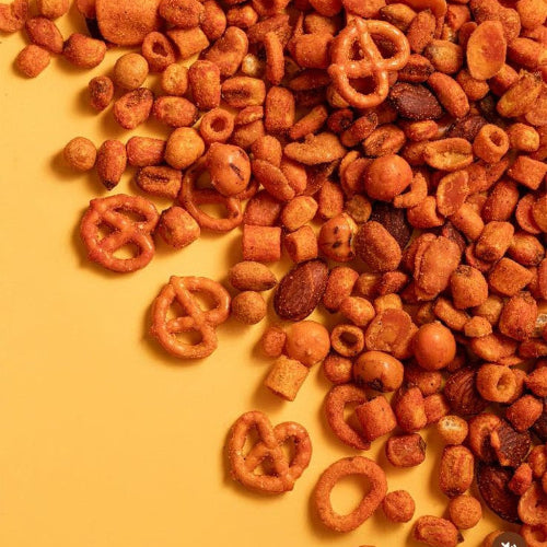 Assorted snack mix including pretzels, nuts, and cereal on a yellow background