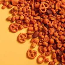 Assorted snack mix including pretzels, nuts, and cereal on a yellow background